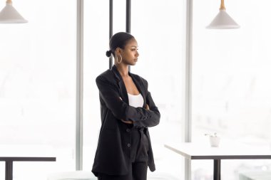 Genç Afrikalı zarif iş kadını birlikte çalışma alanında tek başına duruyor, düşünceli, düşünceli bir ifadeyle mesafeye bakıyor, derin düşüncelere dalmış, karar vermeyi düşünüyor, önemli bir konu hakkında düşünüyor.