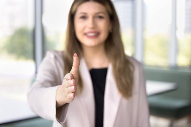 İş kadını el sıkışmak için elini uzatıyor, gülümsüyor, kameraya bakıyor, yakın görüntüyü bulanıklaştırıyor. İş kadını iş birliği teklif ediyor, iş görüşmesine gelen yeni bir çalışana hoş geldin diyor. HR, anlaşma, iş jesti