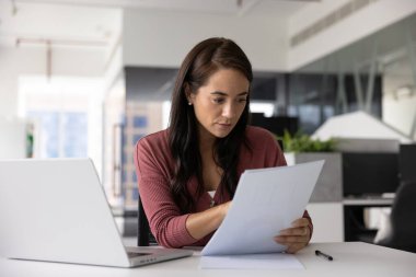 İşyerindeki yasal mali belgeleri okuyan Latin iş kadını laptopuyla raporları analiz ediyor. Sözleşme testi, anlaşma şartları üzerinde çalışan profesyonel analist