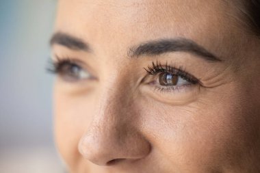 Kahverengi gözlü, gülümseyen, kıvrımlı kirpiklerinde siyah rimel olan orta yaşlı bir kadın. Üst kadın yüzü kesilmiş makro çekim. Model başka tarafa bakıyor, göz bakımı, görme ve güzellik bakımını teşvik ediyor.