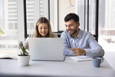 Açık alan ofisinde, ortak online proje üzerinde çalışan iki takım arkadaşı, dizüstü bilgisayardaki yeni programı gözden geçirir, internette içeriği izlerken gülümser, sunumu hazırlar ve verimli iş akışından memnun olurlar.
