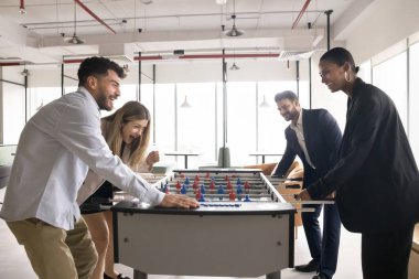 Neşeli iş arkadaşları ofiste masa futbolu oynuyorlar, mutlu görünüyorlar, aşırı sevinçliler, çığlık atıyorlar, iş yerinde kaygısız öğle yemeği molası veriyorlar. Birlik, takım oluşturma etkinliği