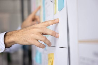 İşletme proje yöneticisi, beyaz tahtaya renkli çıkartmalarla bakıyor, yapışkan notlarla çevik yöntemler kullanıyor, iş arkadaşlarıyla görüşüyor, görevleri tartışıyor. Yakın çekim kesilmiş.