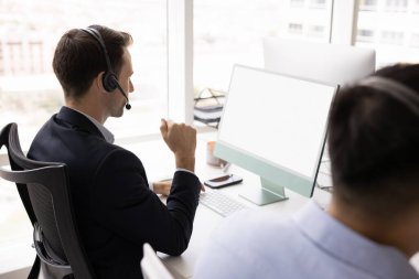Monitörde boş ekranla çalışan, ses çağrısında müşteriyle konuşan, iş iletişimi için modern kablosuz teknolojiyi kullanan çeşitli erkek müşteri destek yöneticilerinin arka görünümü