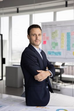 Başarılı İspanyol şirketi CEO 'su profesyonel iş portresi. Ofiste dikey portre için poz veren kendine güvenen Latin işadamı, kollarını güven jestine sarmış, kameraya bakıyor.