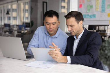 Proje üzerinde birlikte çalışan iki farklı şirket yöneticisi, dijital cihazları takım çalışması, kurumsal tartışma, tablet bilgisayarda online web ürün sunumu izleme