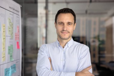 Pozitif yakışıklı İspanyol CEO 'su elleri bağlı, güven jesti yapıyor, yapışkan notlarla güvertede duruyor, kameraya bakıyor. İş projesi lideri, ürün yöneticisi portresi