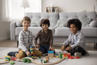 Oyunla bağ kuruyorum. Aile portresi. Üç arkadaş canlısı çok kültürlü küçük çocuk. Üvey kardeşler yerde oturmuş renkli ahşap demiryolu yapımında dikkatleri dağılmış kameralara bakıyorlar.
