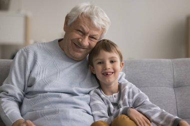 Nesiller arasında aile sevgisi ve sıcaklık. Mutlu aile portresi, mutlu yaşlı büyükbaba rahat koltuğa otur ve kameraya bak, gülümseyen 6-7 yaşındaki torun.