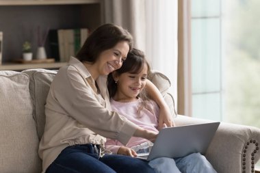 Dijital boş zaman dilimi. Dost canlısı ebeveyn ve çocuk annesi küçük kız hafta sonunu kanepede oturup not defteri kullanarak öğrenme ve eğlenme aracı ile geçiriyor. Anne çocuğuna uygulamada çalışmayı öğretiyor.