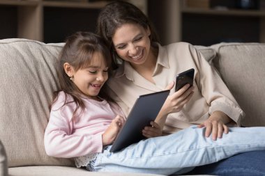 Aletlerle boş zaman. Bekar bir üvey annenin gülümseyen ailesi, evlatlık çocuk rahat koltukta dijital cihazlarla eğleniyor tablet ve akıllı telefon arasındaki fotoğraf videolarını paylaşıyor.