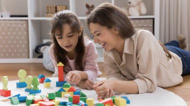 Hayallerin şehrini inşa etmek. Sevgi dolu anne, dadı oyuncak inşaatı ile oynuyor. Küçük kız, rahat oyun odasının zemininde yatıyor. Komik, renkli bir kasaba yaratıyor.