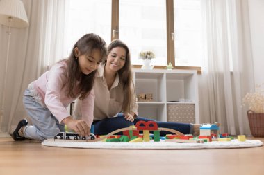 Bağ kurma zamanı ve yaratıcı oyun. Mutlu aile, genç anne, küçük kız, oturma odasının sıcak zemininde oynuyor. Oyuncak trenleri, renkli tuğlalarla dolu şehir trenleri geziyor. Hikayelerin eğlenceli olduğunu hayal edin. Boşluğu kopyala