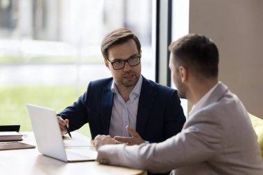 Masada oturmuş, takım çalışmasını tartışan, dizüstü bilgisayar paylaşımı fikirlerini paylaşan, modern çalışma alanındaki resmi toplantı sırasında iş konuşması yapan iki beyaz erkek arkadaş.