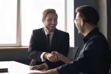 Neşeli, kendinden emin iş adamları ofis masasında el sıkışıyor, kapanış toplantısı, sözleşme, başarılı proje, konuşuyor, gülümsüyor, gülüyor. Yönetici müşteriye el sıkışma veriyor