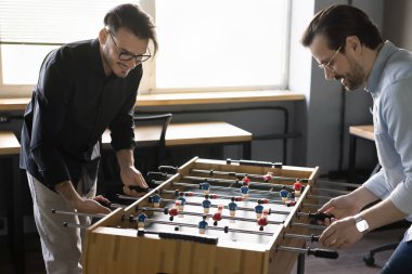 Pozitif heyecanlı iş arkadaşları aktif molada, ofiste eğleniyorlar. Masa futbolu oynayan iki işadamı, futbol maçında yarışıyor, gülümsüyor, eğleniyor, gülüyor.