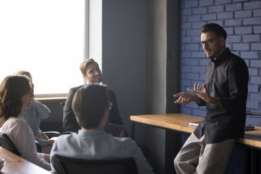 Ciddi yakışıklı genç proje lideri ekiple konuşuyor, fikirler sunuyor, iş planı, strateji tartışıyor, çalışanlarla beyin fırtınası yapıyor. Danışman, koç sunum dersi