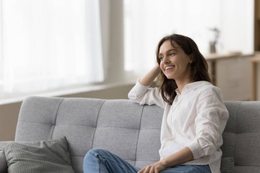 Mutlu, genç bir kadın rahat koltukta dinleniyor, tembel, neşeli, keyfine bakıyor, evde rahat, düşünüyor, hayal ediyor, planlıyor, gülümsüyor, gülümsüyor, başını arkaya yaslıyor.