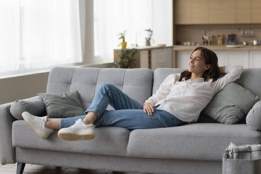 Evdeki kanepede dinlenen, arkasını yaslayan, temiz hava soluyan, pencereden dışarı bakan, dinlenen, düşünen, keyfine bakan, pozitif, huzurlu genç bir kadın. Tam boy çekim