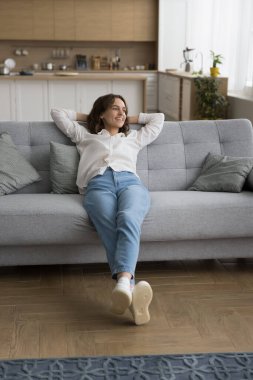 Neşeli, kaygısız ev sahibi kız evdeki yumuşak koltukta dinleniyor, vücudu kanepede geriyor, rüya gibi bir gülümsemeyle başka tarafa bakıyor, düşünüyor, plan yapıyor, keyif alıyor, rahatlıyor, rahatlıyor.