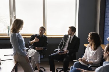 Bir grup çalışan ofis toplantı odasında toplanıp, iş projesini tartışıyor, beyin fırtınası yapıyor, fikirler sunuyor, kıdemli bayan patronla, iş lideriyle, akıl hocasıyla konuşuyor.