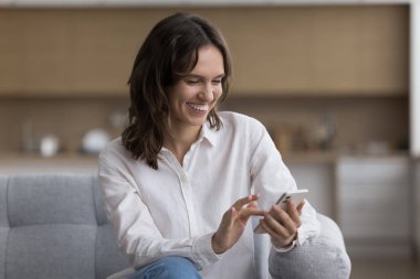 Neşeli, genç cep telefonu kullanıcısı bir kadın. Alet üzerinde yazıyor, sohbet ediyor, video görüşmesi yapıyor, internet iletişimi için akıllı telefondaki uygulamayı kullanıyor, gülümsüyor, gülüyor, ekrana bakıyor.