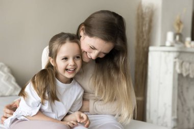 Neşeli genç anne, küçük bebekle yatakta oynuyor, sarılıyor, gıdıklıyor, gülüyor, tatlı küçük kızını kucağında tutuyor, anneliğin tadını çıkarıyor, aile eğlencesi, komik aktiviteler.