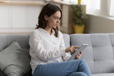 Evde kanepede oturan, kitap okuyan, internetten alışveriş yapan, uzak çalışma için internet uygulaması kullanan, kablosuz iletişim, dokunmatik ekran