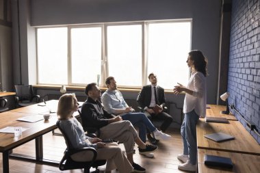 Nişanlı genç işletme koçu kız eğitim veriyor, çalışma grubuna seminer veriyor. Yönetici, küçük meslektaşlar ekibinin önünde konuşuyor, proje planı sunuyor, toplantı stratejisi