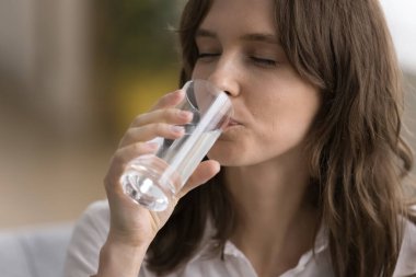 Susamış genç bir kadın, temiz, soğuk suyu kapalı gözlerle içiyor, şeffaf camlar tutuyor, sağlıklı su dengesini sağlıyor, beslenme ve diyetle ilgileniyor. Yakın çekim.