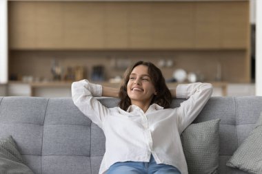 Yumuşak kanepede uzanan, başka tarafa bakan, hayal eden, düşünen, gülümseyen mutlu, güzel genç kadın. Memnuniyet duyan ev sahibi, apartman sahibi yeni evin tadını çıkarıyor.