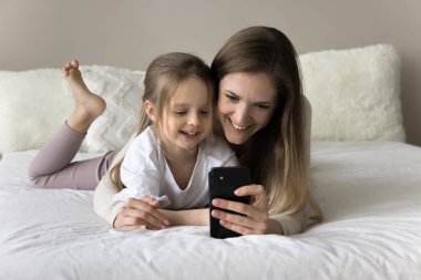 Sevgi dolu bir anne akıllı telefondan şirin bir kıza çevrimiçi içerik gösteriyor. Mutlu anne ve küçük kızı evde dinleniyor, cep telefonuyla öğrenme uygulamasını kullanıyor, video konuşmaları yapıyor, gülüyor.