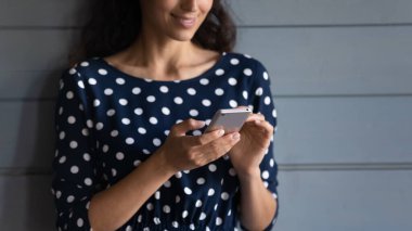 Akıllı telefon kullanan, mesaj yazan, ekranda yazan, gri ahşap duvarda duran, arka planda izole edilmiş, mutlu kadın sohbeti ya da internetten alışveriş yapan,