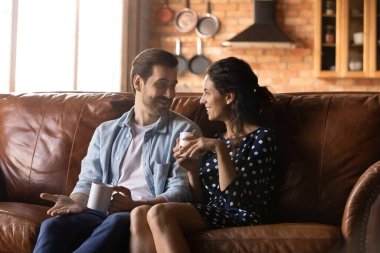 Mutlu çift sohbet ediyor, bardakları tutuyor, rahat koltuklarda birlikte dinleniyor, sıcak içecekler içiyor, evde çay ya da kahve içiyor, gülümseyen erkek ve kadın boş zamanlardan keyif alıyor, konuşuyor, eğleniyor.