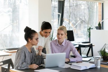 Yoğunlaşmış çok ırklı kadın meslektaşlar laptopta beyin fırtınası ile iş birliği yapıyorlar. Odaklanmış çok ırklı kadınlar bilgisayarda birlikte çalışıyorlar, şirket iş projelerini grup halinde tartışıyorlar..