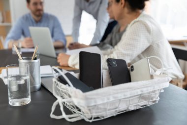 Ofis toplantısında iş adamlarının beyin fırtınası sırasında kutudaki modern akıllı telefonları kapatın. Cep telefonları sepete konur, iş yerindeki çalışanlar brifinginde cep telefonu kullanılmaz..
