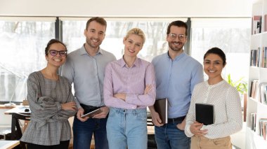 Çeşitli etnik çeşitlilikte gülümseyen iş adamlarının portresi modern ofiste birlik ve güven göstermektedir. Mutlu çok ırklı çalışanlar iş yerindeki kameralara bakıyor. İstihdam kavramı.
