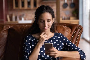 Telefonları, internet uygulamalarını kullanan, evdeki rahat koltukta oturan, telefon ekranına bakan, sosyal ağlarda sohbet eden, online alışveriş yapan, video izleyen, tatmin olmuş bir kadın.