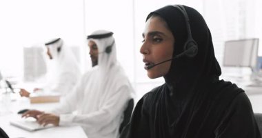 Arap halktan oluşan bir grup, geleneksel Müslüman kıyafeti giymiş teknik destek çalışanları masa başında oturur, müşterilere sorun çözmede, hizmet ile ilgili veya teknik sorunları sohbet yoluyla çözmede yardımcı olurlar.