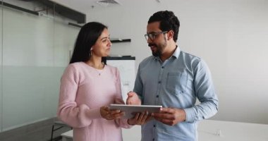 Çok ırklı takım arkadaşları, Hintli kadın ve Arap erkek modern ofisteki tablet aygıtını kullanarak iş ile ilgili konuşmaları yönetiyor, işbirliği içinde tartışmalar yapıyor, proje detayları ve verileri birlikte gözden geçiriyorlar.