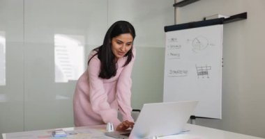 Dizüstü bilgisayarda çalışan Hintli profesyonel kadın, gösterilen tablolar ve grafiklerle masaya yaslanıyor, strateji geliştiriyor, inceleme raporu ya da veri topluyor. Dijital pazarlama, iş akışı, proje yönetimi