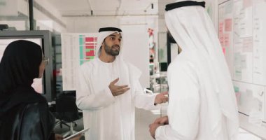 Arap takım arkadaşları geleneksel Müslüman kıyafetleri içinde modern çalışma alanında el sıkışıyor, takım çalışmasını tamamlıyor, işbirliği ve başarılı ortaklıktan memnun oluyorlar. Anlaştık, arkadaşlık.