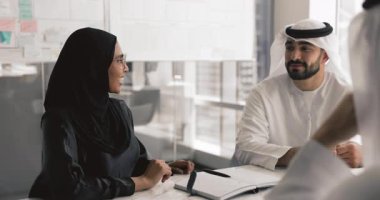 Abaya 'daki gülümseyen kadın kandora gibi giyinmiş iki erkek takım arkadaşıyla sohbet ediyor, ofiste profesyonel iş toplantısına katılıyor, plan yapıyor, işbirliği yapıyor, fikir ve görüşlerini paylaşıyor.