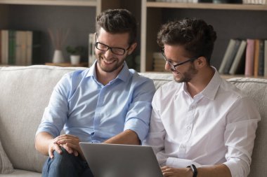 Dijital teknoloji ve eğlence. Neşeli gülen gen z erkek kardeşler ikiz kardeş hipsterlar oturma odasındaki kanepede rahatlar komedi videoları izlemek için not defteri kullanın sosyal medyada komik mimler tartışın şakalar paylaşın