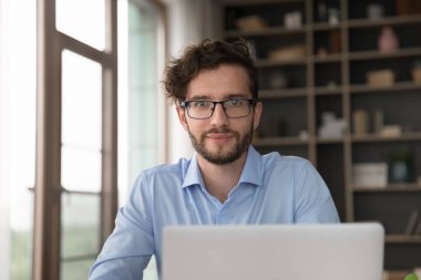 Yaratıcı profesyonel. Vesikalık portre mutlu motivasyonlu milenyum erkek işçi öğrenci ofis masasına oturup not defteri ekranının üstündeki kameraya bakın iş ilhamından esinlenerek işinizde iyi olmaktan gurur duyun.