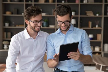 Dijital projede işbirliği. İki tane gülümseyen yetişkin ikiz kardeş modern tabletle oturma odasında duruyor. Çevrimiçi çalışma projesi bilgileri hakkında tartışıyorlar. Ekran içeriğine bakıyorlar.