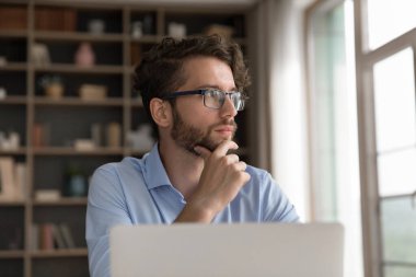 Sorun çözmeye odaklanmış. Düşünceli Gen Z-man ofis çalışanı girişimci öğrenci dikkat dağıtıcı pencere bakmak defter ekran analiz verileri araştırma anlaşması için görselleştirme rapor planı