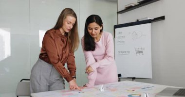 İki çekici çok ırklı genç bayan takım arkadaşı, proje detayları ve satış sonuçlarını göz önünde bulundurarak, ofiste beyin fırtınası yapan sunum ya da raporu hazırlıyor. Takım çalışması.