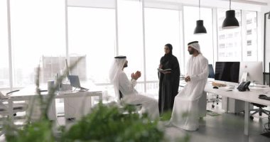 Geleneksel Müslüman kıyafetleri giymiş üç Arap takım arkadaşı modern çalışma sahasında tartışıyorlar, müşteri görüşlerini planlıyorlar, gözden geçiriyorlar, ticari öneriler, müzakerelere hazırlanıyorlar.