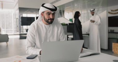 Ofiste çalışan Arap işadamı dizüstü bilgisayarla masaya oturmuş, önemli notlar alıyor, grafikleri grafiklerle gözden geçiriyor, alınan bilgileri karşılaştırıyor, istatistiksel verilere dayalı rapor hazırlıyor